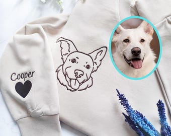 May include: Beige sweatshirt featuring an embroidered dog portrait and the name "Cooper" with a black heart. A circular photo of a white dog is on the right. The dog portrait is in brown thread.