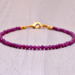 Puede incluir: Una delicada pulsera con pequeñas gemas redondas de color rosa intenso. La pulsera se asegura con un cierre dorado. Las gemas son de un tono rosa vibrante.