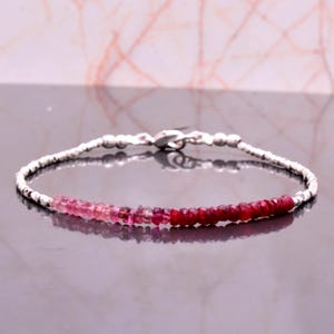 Puede incluir: Una delicada pulsera con una cadena de plata y una serie de pequeñas piedras preciosas facetadas. Las piedras preciosas transitan del rosa claro al rojo intenso. La pulsera tiene un cierre seguro. Aproximadamente 18 cm de largo.