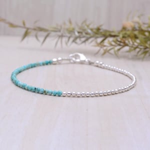 Può includere: Un delicato braccialetto con perline turchesi e piccole perline d'argento. Il braccialetto ha una chiusura argentata. Le perline turchesi si trasformano in perline d'argento.