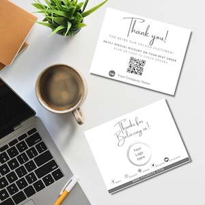 May include: Two white business cards with text, "Thank you!" and "Thanks for Believing in!" are on a white surface. A laptop, coffee cup, pen, and small plant are also visible. The cards include a QR code and social media icons.