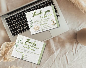May include: Two white thank you cards with green accents and botanical illustrations are displayed on a laptop keyboard. The cards feature text that reads "Thank you" and "Thanks" with contact information and social media handles.