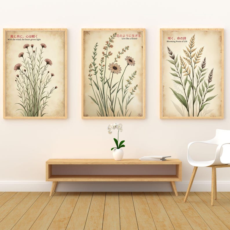 K&ouml;nnte beinhalten: Drei gerahmte botanische Drucke mit floralen Illustrationen in ged&auml;mpften T&ouml;nen. Jeder Druck zeigt japanischen Text und englische &Uuml;bersetzungen. Die Drucke werden &uuml;ber einem Holzkonsolentisch mit einer wei&szlig;en Orchidee und einem modernen wei&szlig;en Stuhl ausgestellt.