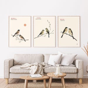 K&ouml;nnte beinhalten: Set aus drei gerahmten Kunstdrucken mit Illustrationen von V&ouml;geln auf &Auml;sten. Jeder Druck hat einen cremefarbenen Hintergrund mit japanischem Text und englischen &Uuml;bersetzungen. Die Drucke werden &uuml;ber einem beigen Sofa mit h&ouml;lzernen Beistelltischen ausgestellt.