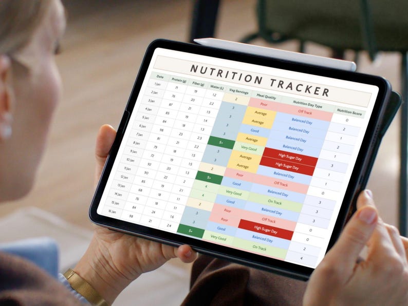 May include: A person holds a black tablet displaying a "NUTRITION TRACKER" spreadsheet. The tracker shows columns for date, protein, fiber, water, veg servings, meal quality, nutrition day type, and nutrition score. A white stylus rests on the tablet.