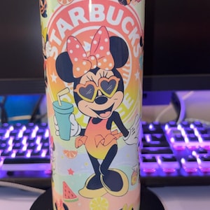 May include: A cylindrical tumbler featuring a colorful graphic of Minnie Mouse wearing heart-shaped sunglasses and a polka-dot bow. The design includes the text STARBUCKS, watermelon slices, citrus fruit segments, and small stars against a pastel gradient background.