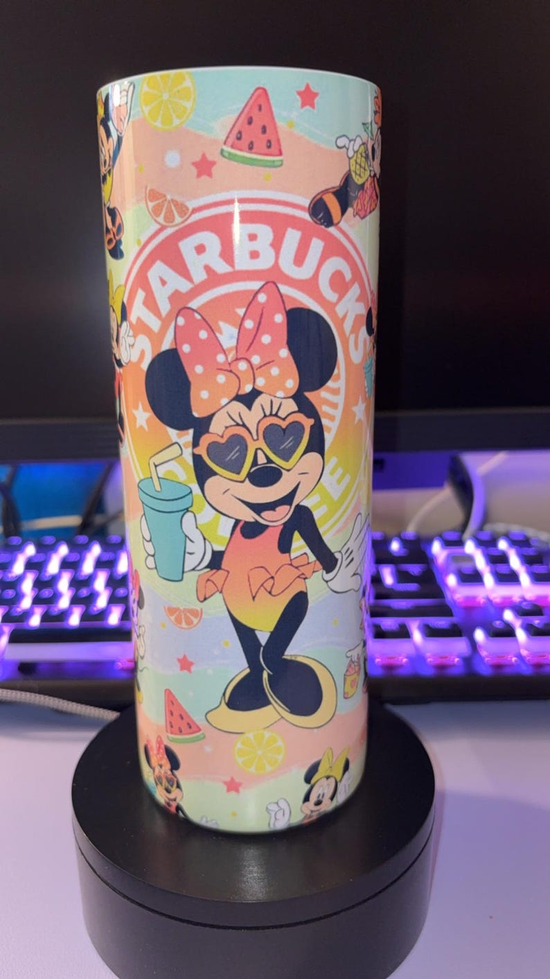 May include: A cylindrical tumbler featuring a colorful graphic of Minnie Mouse wearing heart-shaped sunglasses and a polka-dot bow. The design includes the text STARBUCKS, watermelon slices, citrus fruit segments, and small stars against a pastel gradient background.