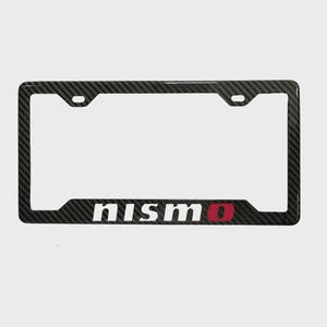 May include: Black carbon fibre number plate frame featuring the word "nismo" in white and red lettering. The frame is rectangular with rounded corners and mounting holes.