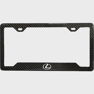 May include: Black carbon fiber license plate frame with the Lexus logo in white. The frame has a woven texture and a rectangular shape with rounded corners. The Lexus logo is centered at the bottom.