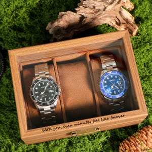 May include: A wooden watch display case with two watches. One watch has a black face and the other has a blue face. The text on the case reads "With you, even minutes feel like forever."
