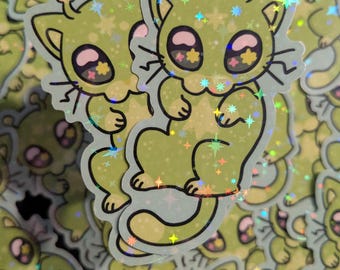 May include: A collection of stickers featuring a cartoon cat-like alien character in shades of green and yellow. The stickers have a holographic, glittery finish with star-shaped accents and large, expressive eyes.