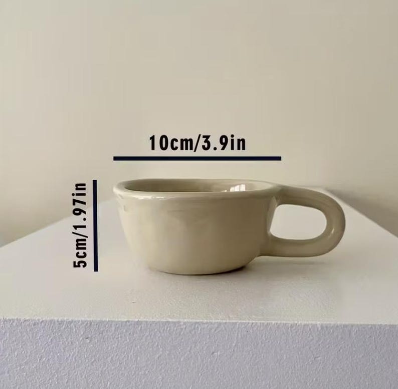 May include: A beige ceramic mug with a rounded body and a thick handle. The mug features printed text indicating dimensions of 3.9 inches in width and 1.97 inches in height, providing a clear visual reference for the size of this drinkware item.