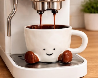 May include: A white ceramic mug with a textured surface, a simple black smiley face, and two brown feet at the base, positioned under a white espresso machine that is dispensing two streams of dark brown coffee into the mug's interior.