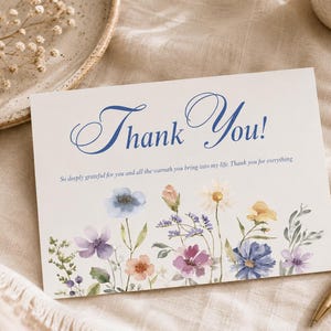 May include: A rectangular white greeting card featuring the blue script text Thank You! and the smaller printed message So deeply grateful for you and all the warmth you bring into my life. Thank you for everything, with watercolor wildflowers.