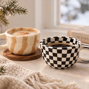 May include: Two ceramic mugs with rounded handles. One mug features a beige and white vertical striped pattern and contains a light-colored beverage. The other mug displays a black and white checkered pattern and contains a dark-colored beverage.