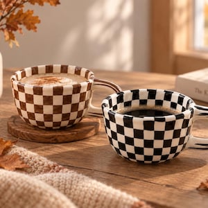 May include: Two ceramic mugs with a checkered pattern. One mug features a brown and white checkerboard design filled with a light-colored beverage, while the other displays a black and white checkerboard pattern filled with dark coffee.