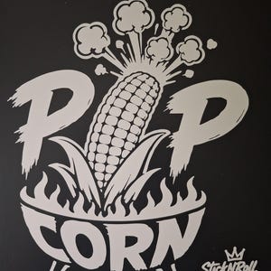 Könnte beinhalten: Ein weißer Vinyl-Aufkleber auf schwarzem Hintergrund mit einer Grafik eines Maiskolbens, der aus einer Schüssel mit Flammen an der Basis herausplatzt. Der Text lautet POP CORN in großen Buchstaben, mit einem kleinen StickNRoll-Logo mit Krone unten rechts.