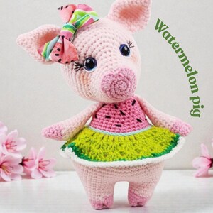 Op de afbeelding: Een handgemaakte gehaakte varkenspop met een watermeloen-thema jurk en strik. Het varken is roze met een roze en groene jurk, een watermeloen schijf ontwerp en een kleurrijke strik. De tekst "Watermelon pig" staat aan de rechterkant.