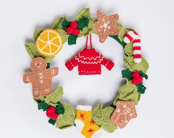 May include: A handmade Christmas wreath featuring crocheted elements. The wreath includes a gingerbread man, a slice of orange, a red sweater ornament, and a candy cane. Green leaves and red berries are also incorporated into the design, creating a festive holiday decoration.