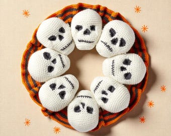 May include: A Halloween wreath featuring eight white crocheted skulls with black facial features. The skulls are arranged in a circle on a wreath with orange and black stripes. Orange star shapes are scattered around the wreath.