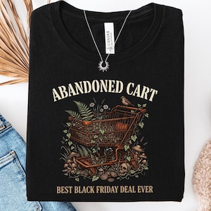 May include: A black t-shirt featuring a graphic of a rusted shopping cart overgrown with ferns, vines, and mushrooms. The text ABANDONED CART appears above the cart, and the text BEST BLACK FRIDAY DEAL EVER is printed below the illustration.