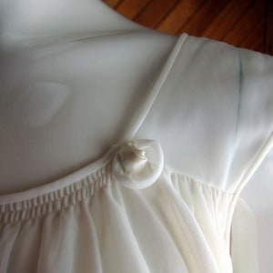 May include: White sheer nightgown with a gathered neckline and a single white satin button at the shoulder.