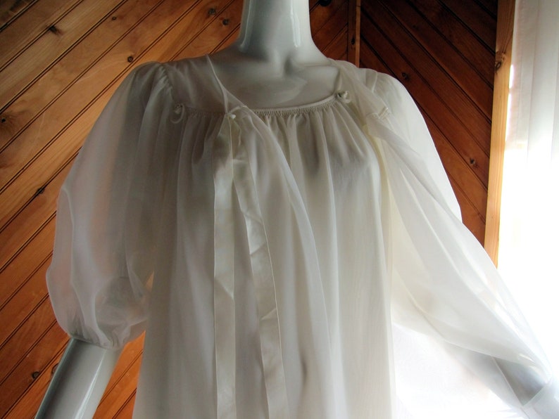 May include: A white sheer nightgown with a gathered neckline and long sleeves. The gown has a tie at the neckline and is made of a lightweight fabric.