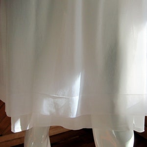 May include: A white, sheer, layered garment with a simple design. The garment is made of a lightweight fabric and has a flowing silhouette.