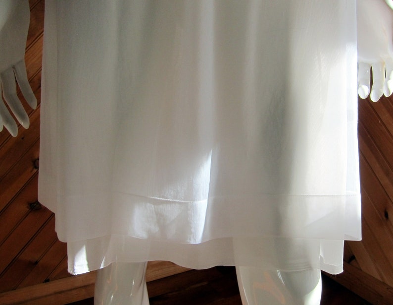 May include: A white, sheer, layered garment with a simple design. The garment is made of a lightweight fabric and has a flowing silhouette.