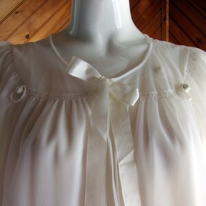 May include: A white sheer robe with a satin ribbon tie and two small buttons on the shoulders.