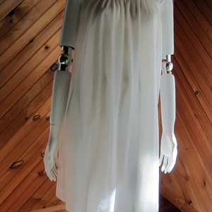 May include: A white, sleeveless, knee-length slip dress with a gathered neckline and a button detail on the shoulder.