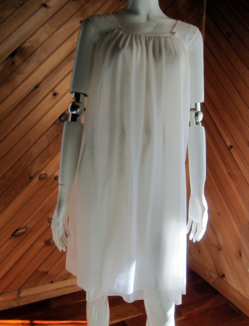 May include: A white, sleeveless, knee-length slip dress with a gathered neckline and a button detail on the shoulder.