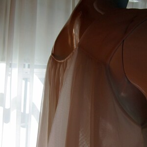 May include: A sheer, light brown slip with a gathered neckline. The slip is made of a soft, flowing fabric and has a delicate, feminine look.
