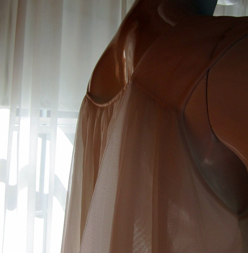 May include: A sheer, light brown slip with a gathered neckline. The slip is made of a soft, flowing fabric and has a delicate, feminine look.