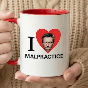Puede incluir: Taza de cerámica blanca con interior y asa rojos. La taza presenta un corazón rojo con un retrato y las palabras "I MALPRACTICE" en negro. La taza la sostiene una persona que lleva un jersey beige.