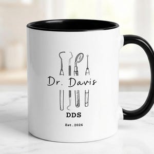 May include: White ceramic mug with a black interior and handle. The mug features a black and white illustration of dental tools, the name "Dr. Davis", the letters "DDS", and the year "Est. 2026".