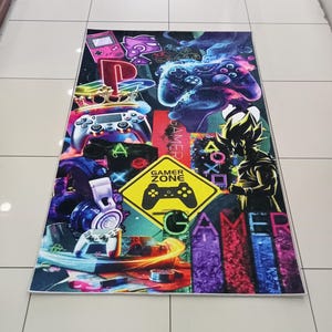 Könnte beinhalten: Ein rechteckiger Gaming-Teppich mit einer Collage aus Videospiel-Controllern, Kopfhörern und einem gelben "Gamer Zone"-Schild. Der Teppich hat ein farbenfrohes Design mit verschiedenen Bildern und dem Wort "GAMER" in großen Buchstaben.