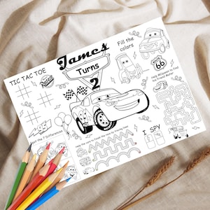 May include: A black and white activity sheet featuring Lightning McQueen from the movie Cars. The sheet includes a tic-tac-toe game, a maze, and other activities. The text "James Turns 2" is displayed at the top. A set of colored pencils is in the foreground.