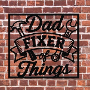 May include: Black metal sign with the words "Dad Fixer of Things" in a decorative font, featuring hammer and wrench illustrations. The sign is set against a red brick wall background.