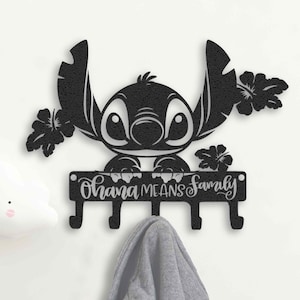 May include: Black metal wall hook featuring a stylized image of Stitch from Lilo & Stitch, with the phrase "Ohana Means Family." The hook has four pegs for hanging items. A gray hoodie hangs from one of the hooks.