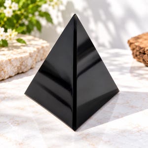 Peut inclure: Une pyramide noire lisse et polie avec un sommet pointu et des bords droits et nets. La surface de l'objet est hautement réfléchissante, montrant de subtils reflets lumineux le long de ses faces géométriques. La base est carrée et les quatre côtés triangulaires se rejoignent en un seul point.