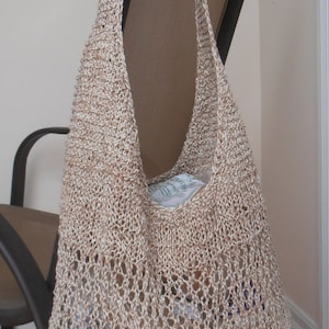 May include: A beige crocheted tote bag with a woven pattern. The bag is hanging on a chair and has a light brown color.