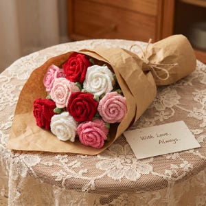 May include: A bouquet of crocheted roses in shades of red, pink, and white, wrapped in brown paper. The bouquet is tied with twine. A small card with the words "With Love, Always." is placed next to the bouquet.
