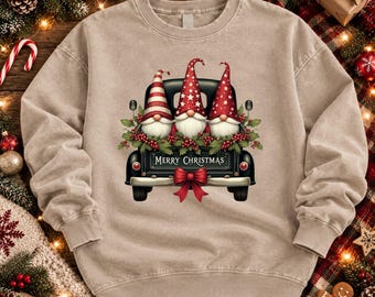 May include: A beige crewneck sweatshirt featuring a graphic of a black vintage truck bed filled with three gnomes wearing red hats, green holly leaves, and red berries. The truck tailgate displays the text Merry Christmas with a red bow.