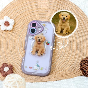 Può includere: Una custodia per telefono color lavanda con una grafica centrale in rilievo di un cucciolo di golden retriever, piccoli adesivi di personaggi Disney e un inserto circolare che mostra lo stesso cucciolo. La parola Disney è stampata sui bordi.