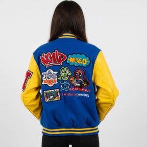 May include: Blue and yellow varsity jacket with multiple colorful patches. The jacket has yellow sleeves and a blue body with a striped collar and cuffs. Patches include cartoon characters and text.
