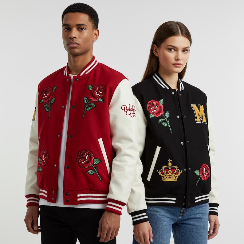 May include: Two varsity jackets, one red and one black, are displayed. The red jacket has white sleeves and rose embroidery. The black jacket has white sleeves, rose and crown embroidery, and a gold "M" patch. Both have striped cuffs and hems.