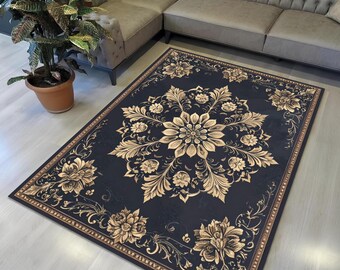 May include: A rectangular, dark blue rug with a large, central floral design in gold. The rug features an ornate border and additional floral motifs. The rug is placed on a light-colored floor, near a gray sectional sofa and a potted plant.