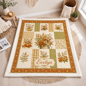 May include: A rectangular throw blanket featuring a patchwork design with autumn-themed illustrations of pumpkins, sunflowers, and foliage in shades of orange, green, and cream. The center includes a decorative label with the name Evelyn printed.