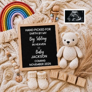 May include: A black felt letter board with white text reading HAND PICKED FOR EARTH BY MY Big Sibling IN HEAVEN Baby JACKSON COMING NOVEMBER 2026, surrounded by a rainbow, a crochet teddy bear, baby booties, wooden blocks, and an ultrasound image.